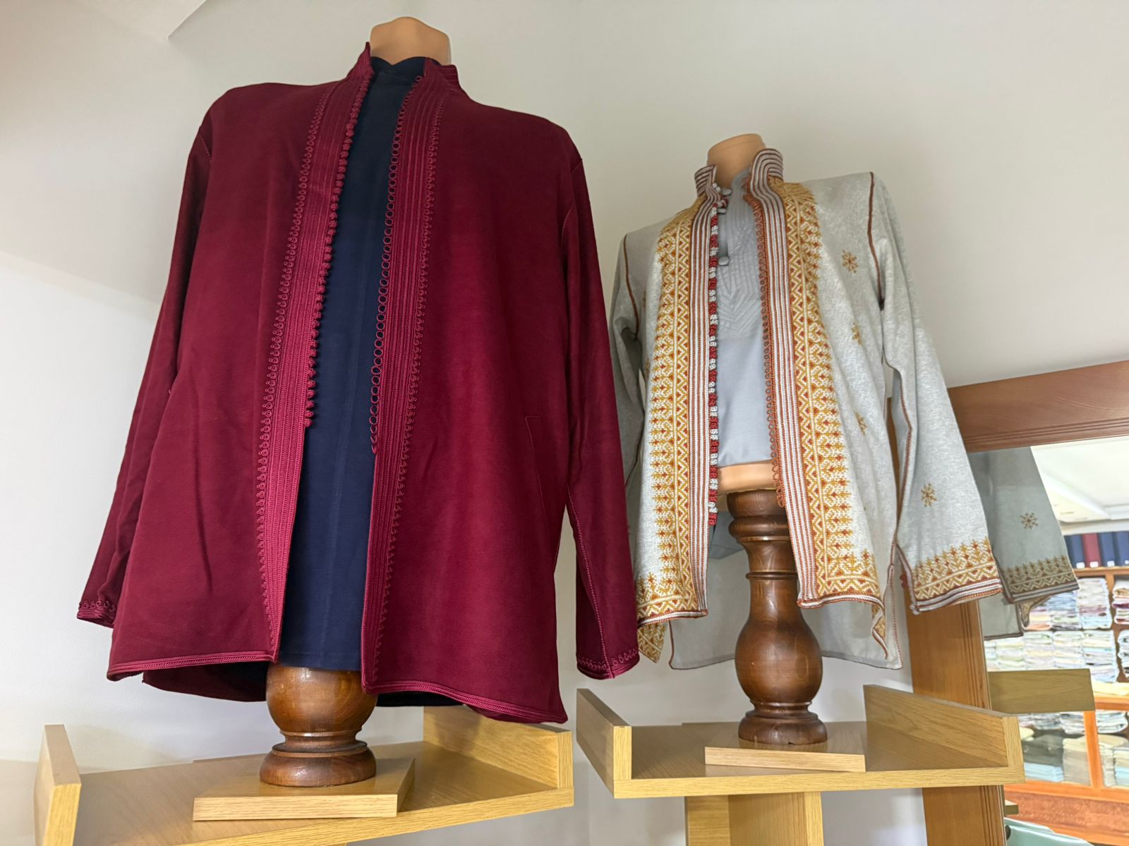 Deux farmlas homme sur bustes — l'une en suédine bordeaux unie, l'autre gris pierre à larges bandes brodées or et rouille de motifs amazighs, Tazi Caftan Marrakech
